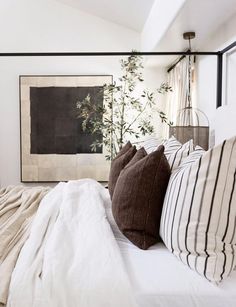 a bed with white sheets and pillows in front of a large painting on the wall