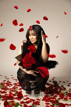 a woman sitting on the ground surrounded by roses and petals with her hands in her hair