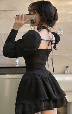 a woman taking a selfie in front of a bathroom mirror wearing a black dress