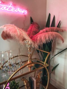 there is a pink neon sign on the wall above some wine glasses and palm trees