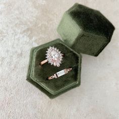 two engagement rings sitting on top of a green velvet ring box in the shape of a hexagon