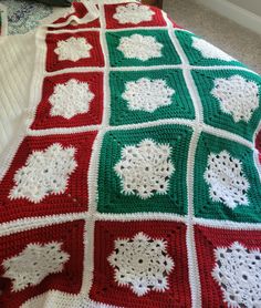 a crocheted afghan is laying on a bed with red and green squares around it