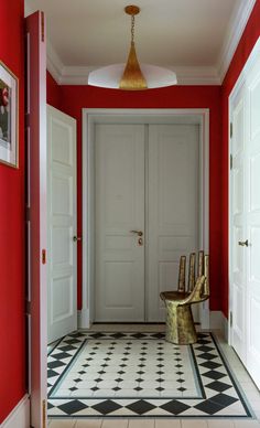 a hallway with red walls and black and white flooring, two chairs on either side of the door