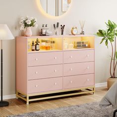 a pink dresser with lots of beauty products on it and a round mirror above it