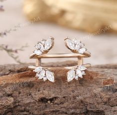 two gold rings with white stones on top of each one, sitting on a piece of wood