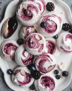 a white plate topped with blueberry rolls covered in icing and berries next to a spoon