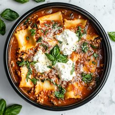 a black bowl filled with pasta and cheese on top of a white countertop next to green leaves