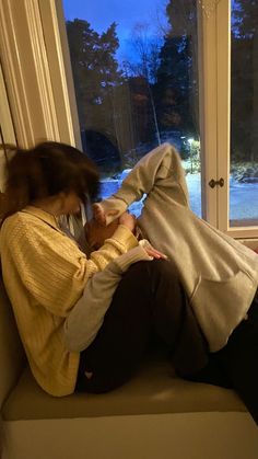 a woman sitting on a window sill looking at her cell phone