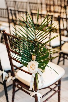 an arrangement of flowers and greenery sits on the back of a chair at a wedding