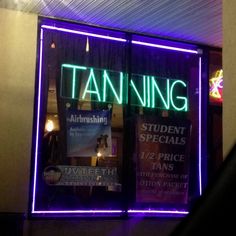 a store front window with neon signs on it's glass and the words tanning lit up