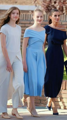 three women walking down the street in dresses and heels, one wearing a blue dress