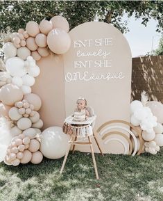 a baby is sitting in a high chair next to balloons and a sign that says,