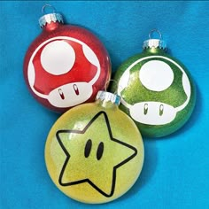 three christmas ornaments on a blue background with one mario mushroom ornament and the other star