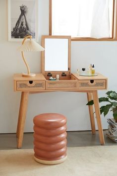 a desk with a mirror, lamp and stool in front of a window next to a potted plant