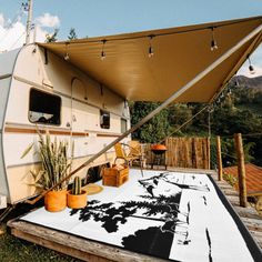 an rv is parked on the grass with its awning open and plants in pots