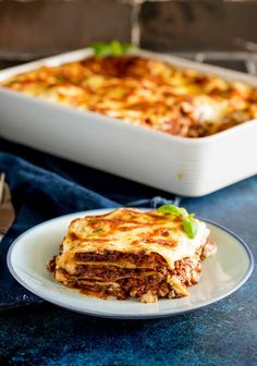 a white plate topped with lasagna next to a pan of lasagna