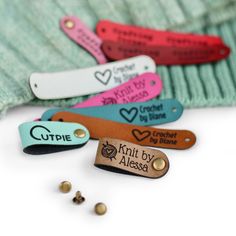 four different colored leather name tags sitting on top of a green sweater next to beads