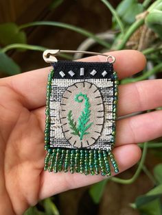 a hand holding a small green and white beaded brooch with a cactus on it