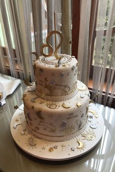 a three tiered white cake with gold stars and numbers on the top, sitting on a table in front of a window