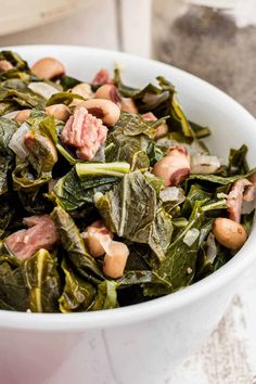 a white bowl filled with collard greens and meats on top of it's sides