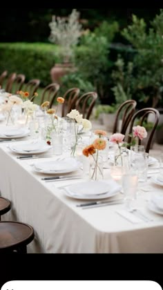 a long table is set with white and orange flowers in vases, plates and silverware