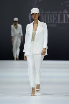 a woman is walking down the runway wearing a white suit and hat with her hands in her pockets