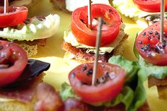 there are many small sandwiches with toothpicks in them on the table, including tomatoes and lettuce