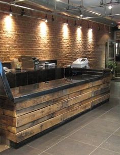 an empty counter in a restaurant with brick walls and lights on the wall behind it