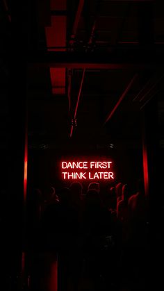 a neon sign that says dance first think later in the middle of a dark room