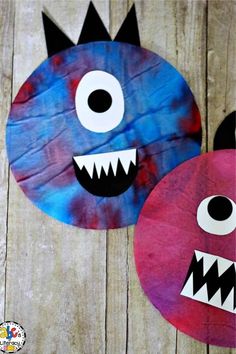 two paper plates decorated with monster faces on wood planks, one is blue and the other is pink