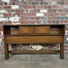 an old wooden bed frame with two drawers on the top and bottom, against a brick wall