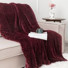 a red blanket sitting on top of a couch next to a vase with flowers in it