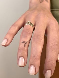 a woman's hand with a ring on it and a flower tattoo on the middle finger