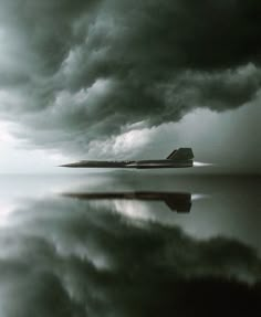 a black and white photo of a house in the middle of water with dark clouds