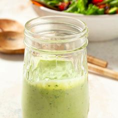 a glass jar filled with green dressing next to a salad