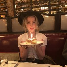 a woman sitting at a table holding a plate with a cake on it in front of her