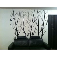 a black leather couch sitting in front of a tree mural