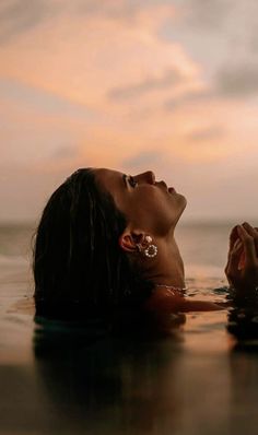 a woman is floating in the water with her hands on her chest and looking up into the sky