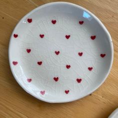 a white bowl with red hearts on it sitting on a table next to a plate