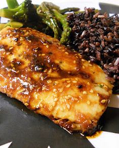 a close up of food on a plate with broccoli and black rice in the background