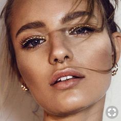 a close up of a person wearing gold eyeliners and piercings on her nose