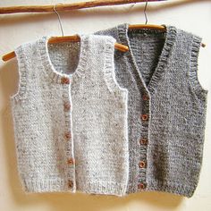 two knit vests hanging on a clothesline next to a wooden hanger with buttons