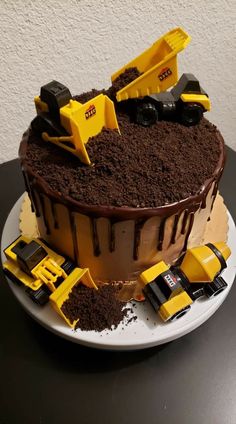 a chocolate cake with yellow construction trucks on top and dirt in the middle, sitting on a plate