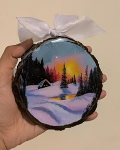 a hand holding a painted ornament with a sunset in the background and snow on the ground