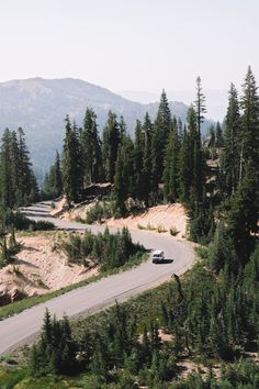 a car driving down a road surrounded by pine trees and mountains in the distance with a mountain range in the background