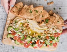 two hands holding a wooden platter filled with nachos and other toppings