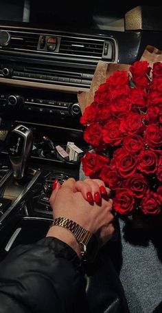 a woman is holding a bouquet of red roses in her hand while she sits in the driver's seat