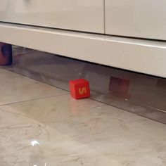 a red block sitting on the ground next to a white cabinet