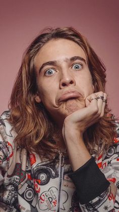 a young man with long hair and blue eyes is posing for a photo in front of a pink background