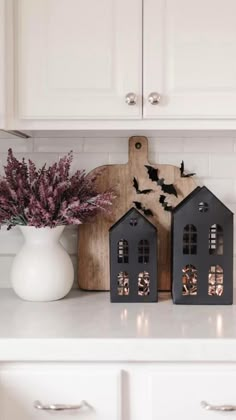 two black houses are sitting on the kitchen counter next to a vase with purple flowers